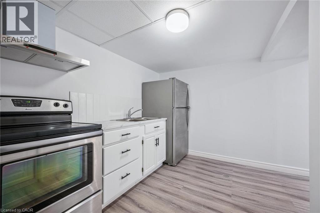 Kitchen featuring appliances with stainless steel finishes, wall chimney exhaust hood, light countertops, white cabinetry, and light wood finished floors - 21 Forest Glen Court, Kitchener, ON - Indoor Photo Showing Kitchen With Double Sink