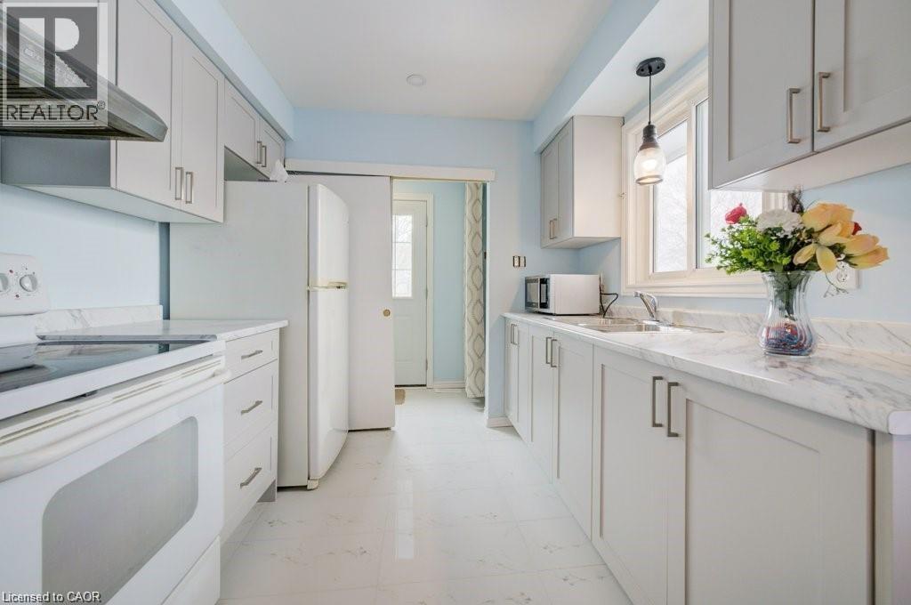 Kitchen with white electric stove, wall chimney range hood, plenty of natural light, and stainless steel microwave - 33 Garland Crescent, London, ON - Indoor Photo Showing Kitchen