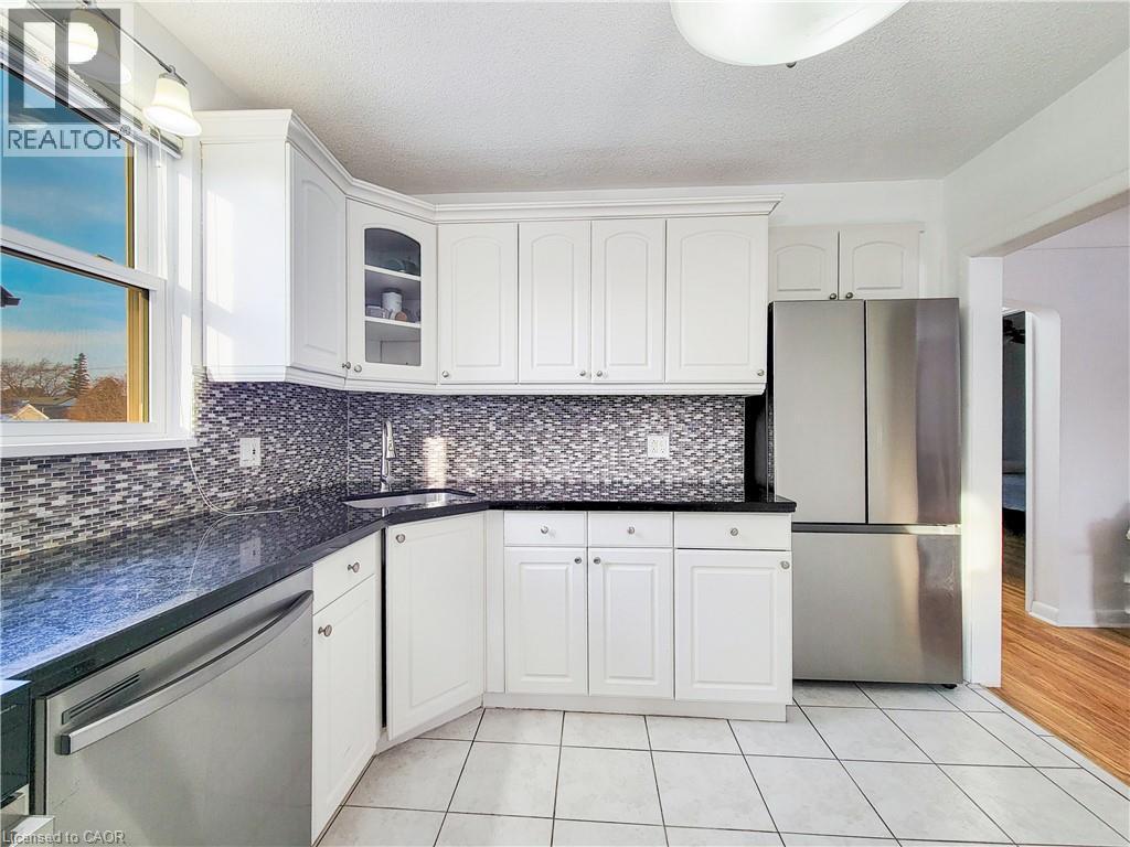 Kitchen with stainless steel appliances, white cabinets, light tile patterned flooring, glass insert cabinets, and a textured ceiling - 773 Queensdale Avenue E, Hamilton, ON - Indoor Photo Showing Kitchen
