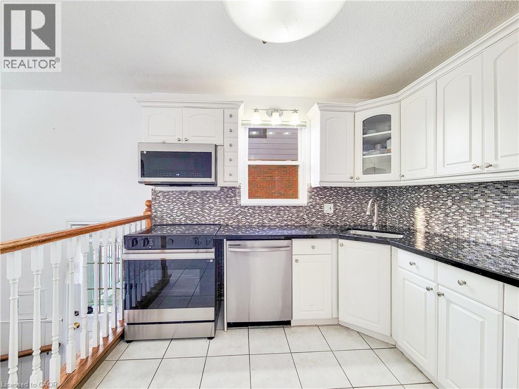 Kitchen featuring appliances with stainless steel finishes, a textured ceiling, white cabinets, glass insert cabinets, and light tile patterned floors - 773 Queensdale Avenue E, Hamilton, ON - Indoor Photo Showing Kitchen
