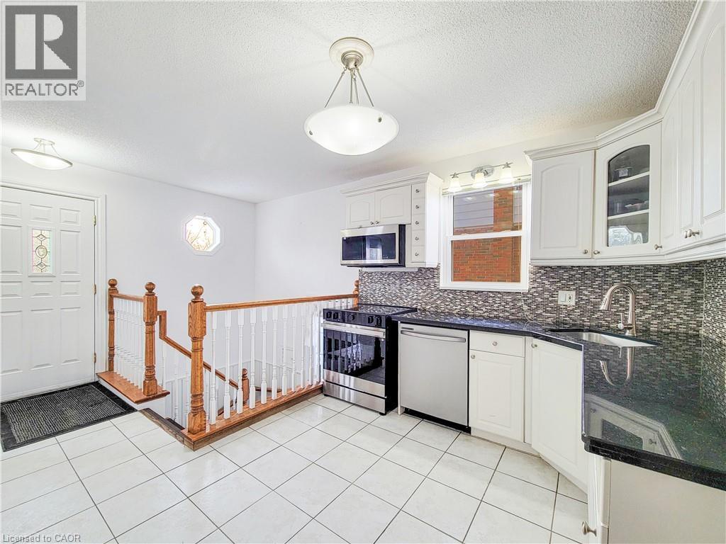 Kitchen featuring stainless steel appliances, a textured ceiling, glass insert cabinets, pendant lighting, and white cabinetry - 773 Queensdale Avenue E, Hamilton, ON - Indoor Photo Showing Kitchen