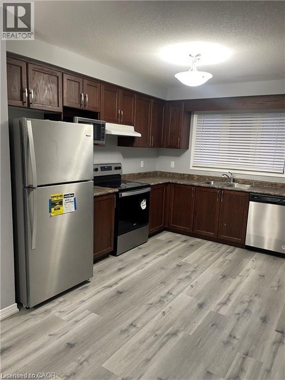 Kitchen featuring stainless steel appliances, dark brown cabinets, dark stone counters, light wood-style flooring, and a textured ceiling - 198 Maitland Street, Kitchener, ON - Indoor Photo Showing Kitchen With Double Sink