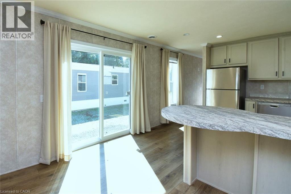 Kitchen featuring appliances with stainless steel finishes, crown molding, dark wood-type flooring, a peninsula, and light stone countertops - 1085 Concession 10 Road W Unit# 23, Flamborough, ON - Indoor Photo Showing Kitchen