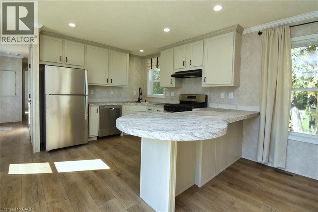 Kitchen featuring a peninsula, light countertops, appliances with stainless steel finishes, dark wood-style flooring, and under cabinet range hood - 1085 Concession 10 Road W Unit# 23, Flamborough, ON - Indoor Photo Showing Kitchen