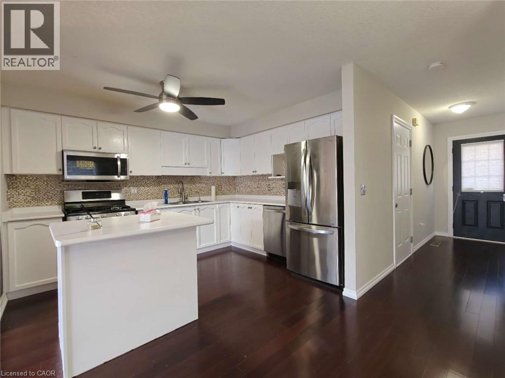 Kitchen with appliances with stainless steel finishes, white cabinetry, tasteful backsplash, dark wood-type flooring, and a kitchen island - 563 Dansbury Drive, Waterloo, ON