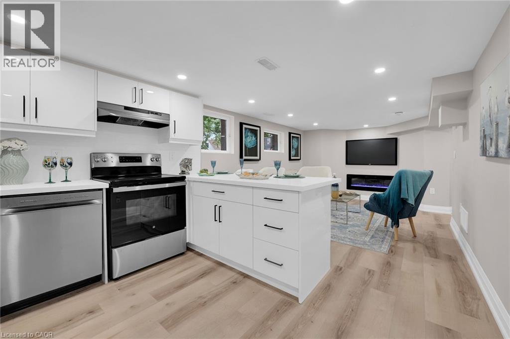 Kitchen featuring a peninsula, appliances with stainless steel finishes, white cabinetry, recessed lighting, and a glass covered fireplace - 174 East 34Th Street, Hamilton, ON - Indoor Photo Showing Kitchen With Upgraded Kitchen