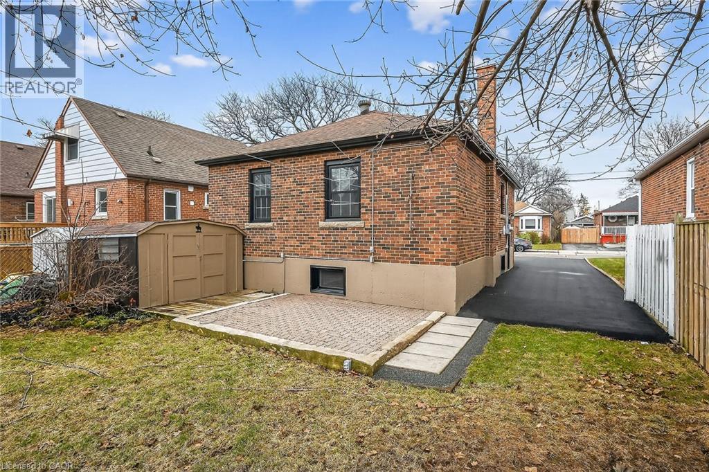 Rear view of house featuring brick siding, a shed, a chimney, a patio area, and roof with shingles - 174 East 34Th Street, Hamilton, ON - Outdoor