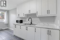 Kitchen with sink, white cabinetry, light stone counters, and a baseboard heating unit -