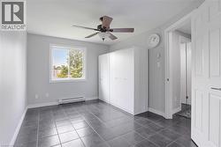 Unfurnished bedroom featuring a baseboard heating unit, dark tile patterned flooring, a ceiling fan, baseboards, and a closet -
