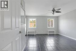 Empty room with a baseboard heating unit, ceiling fan, dark tile patterned floors, and baseboards -