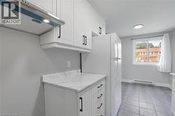 Kitchen featuring white cabinetry, a baseboard radiator, light stone counters, and range hood -