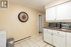 Kitchen with a baseboard heating unit, stainless steel microwave, white cabinetry, white dishwasher, and light tile patterned flooring -