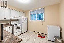 Kitchen featuring white appliances, dark countertops, white cabinets, and baseboard heating -