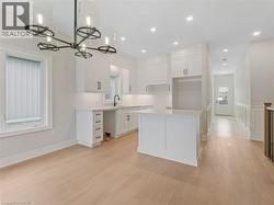 Kitchen featuring a center island, a sink, a chandelier, light wood-style floors, and white cabinetry -
