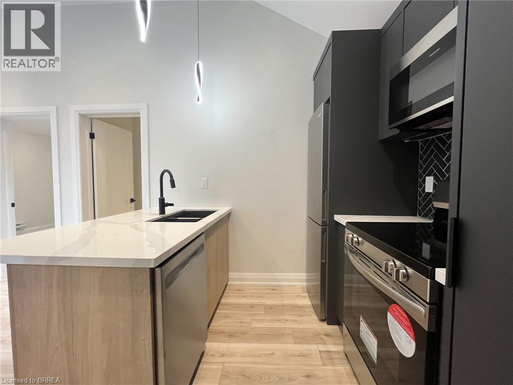 Kitchen with stainless steel appliances, light stone countertops, light wood-style floors, modern cabinets, and a peninsula - 110 Deschene Avenue, Hamilton, ON - Indoor Photo Showing Kitchen With Double Sink