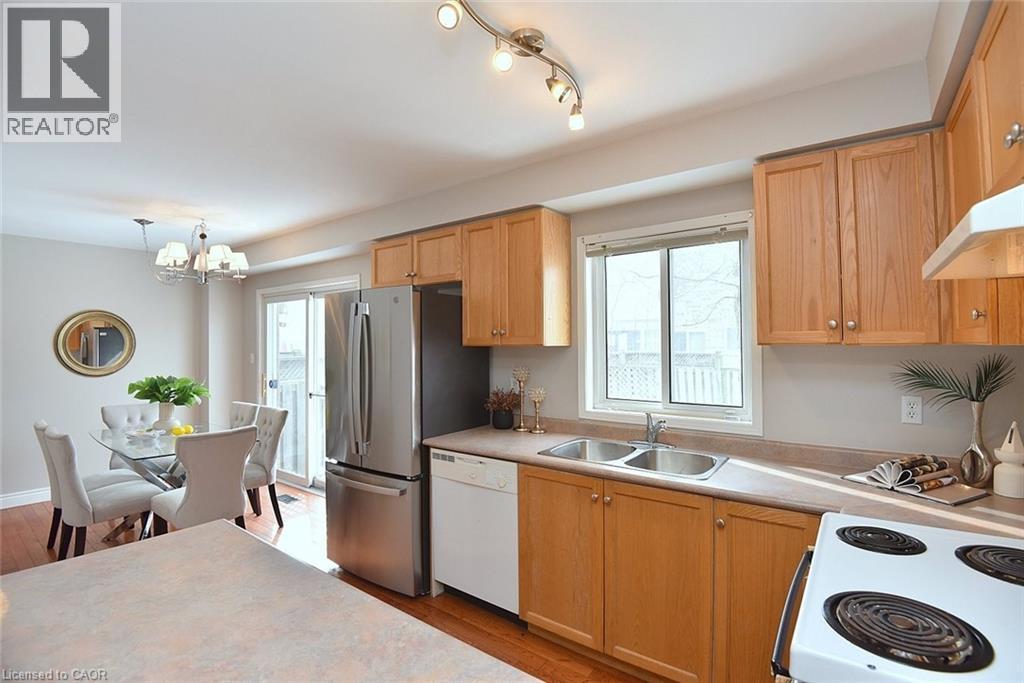 Kitchen with white appliances, light countertops, light wood-style floors, a chandelier, and healthy amount of natural light - 2258 Empire Crescent, Burlington, ON - Indoor Photo Showing Kitchen With Double Sink
