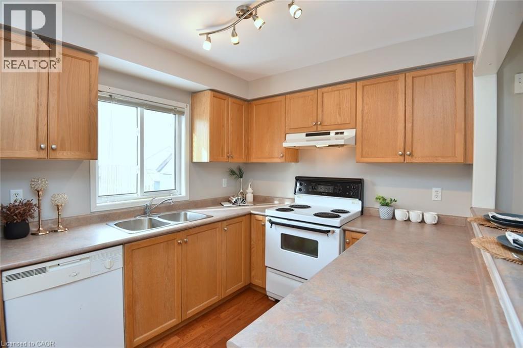 Kitchen with white appliances, light countertops, under cabinet range hood, light wood-style floors, and light brown cabinetry - 2258 Empire Crescent, Burlington, ON - Indoor Photo Showing Kitchen With Double Sink