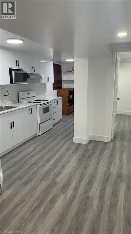 Kitchen with white cabinets, white range with electric cooktop, light countertops, light wood-style floors, and stainless steel microwave - 18 Ingleside Drive, Kitchener, ON - Indoor Photo Showing Kitchen