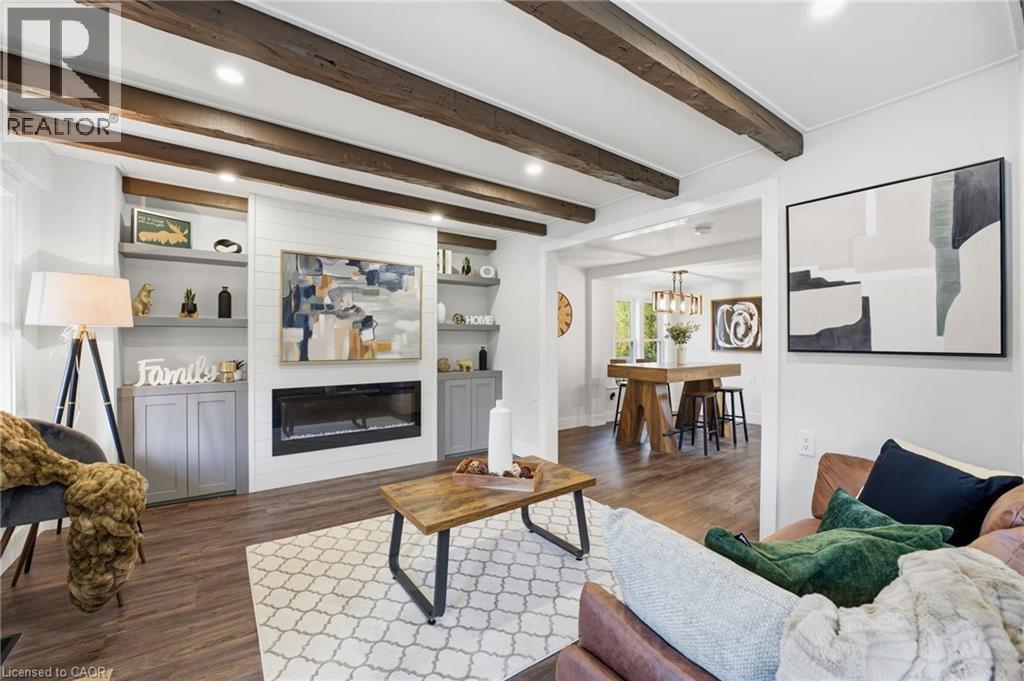 Living room with beam ceiling, a glass covered fireplace, dark wood finished floors, recessed lighting, and built in shelves - 4255 William Street, Beamsville, ON - Indoor Photo Showing Living Room With Fireplace