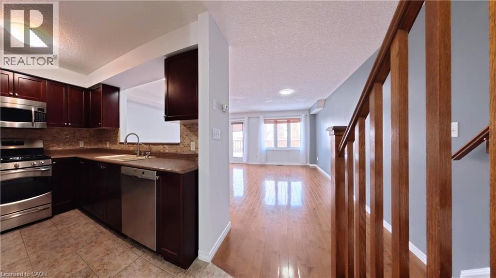 Kitchen with stainless steel appliances, dark brown cabinetry, a textured ceiling, and decorative backsplash - 919 Zeller Crescent, Kitchener, ON - Indoor Photo Showing Kitchen