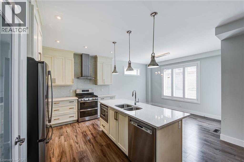 Kitchen featuring stainless steel appliances, light stone countertops, wall chimney range hood, decorative backsplash, and dark wood finished floors - 2527 Holbrook Drive, London, ON - Indoor Photo Showing Kitchen With Double Sink With Upgraded Kitchen