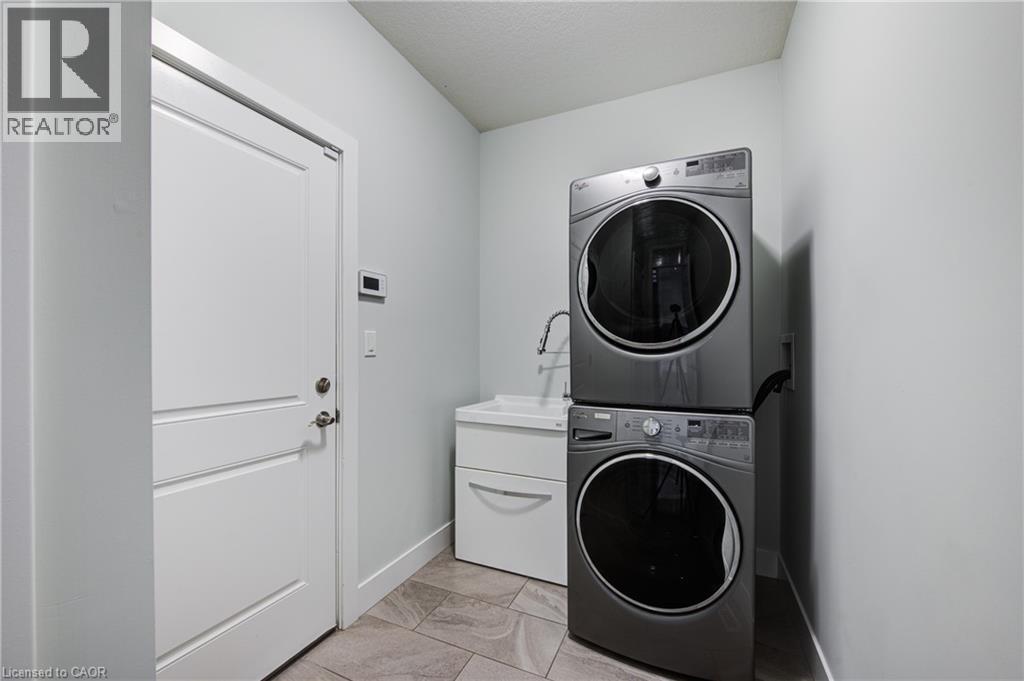Laundry room featuring stacked washing machine and dryer and light marble finish flooring - 2527 Holbrook Drive, London, ON - Indoor Photo Showing Laundry Room