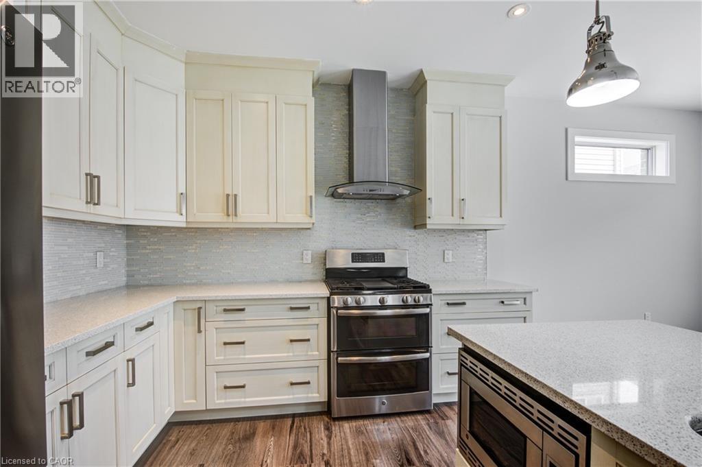 Kitchen featuring stainless steel appliances, wall chimney exhaust hood, decorative backsplash, light stone counters, and pendant lighting - 2527 Holbrook Drive, London, ON - Indoor Photo Showing Kitchen