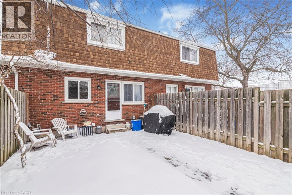 Snow covered back of property with mansard roof, a fenced backyard, roof with shingles, and brick siding - 48 Riverdale Drive Unit# 2, Hamilton, ON - Outdoor With Exterior