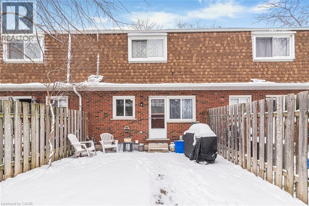 Snow covered rear of property featuring mansard roof, a fenced backyard, a shingled roof, and brick siding - 48 Riverdale Drive Unit# 2, Hamilton, ON - Outdoor With Exterior