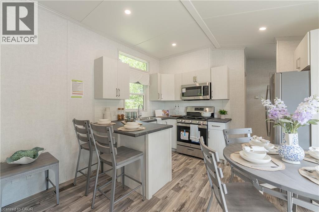 Kitchen with dark countertops, stainless steel appliances, light wood finished floors, a breakfast bar area, and a peninsula - 85 Hutchinson Beach Road Unit# B56, Huntsville, ON - Indoor