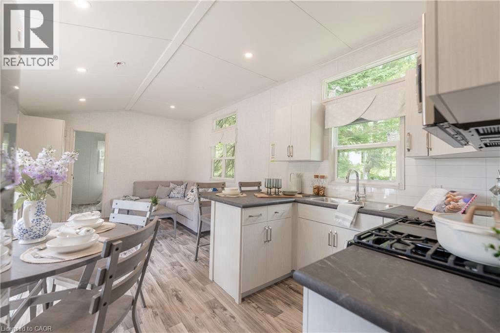 Kitchen with light wood-style floors, vaulted ceiling, backsplash, a peninsula, and white cabinets - 85 Hutchinson Beach Road Unit# B56, Huntsville, ON - Indoor