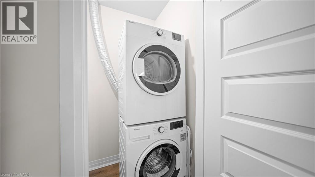 Washroom with stacked washer / drying machine and wood finished floors - 610 Farmstead Drive Unit# 304, Milton, ON - Indoor Photo Showing Laundry Room