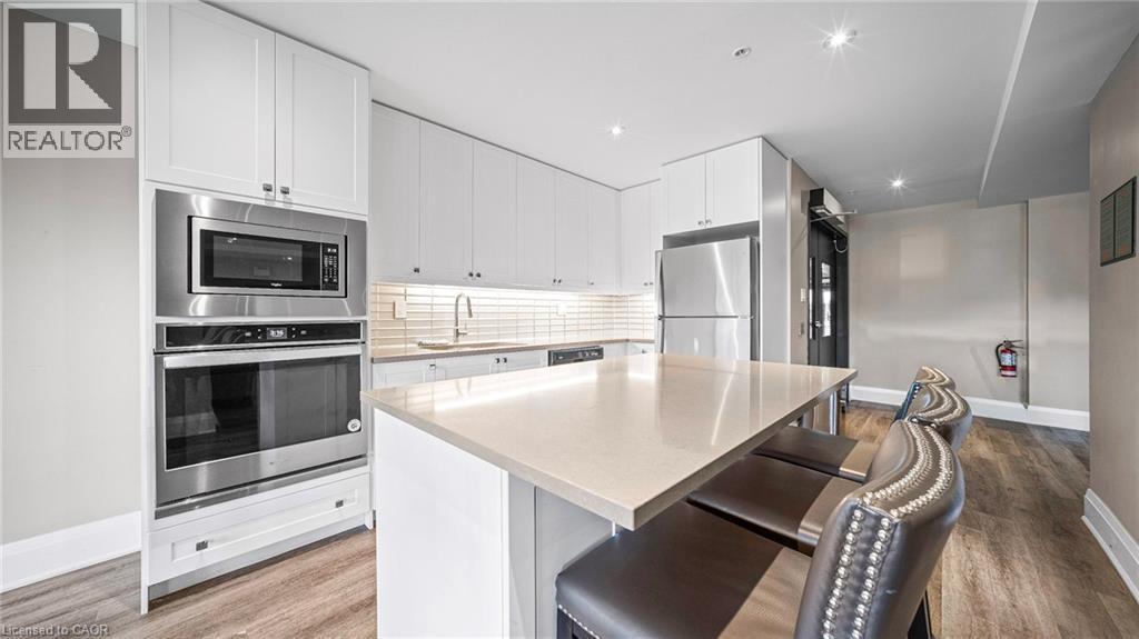 Kitchen with decorative backsplash, a kitchen bar, appliances with stainless steel finishes, white cabinets, and light stone counters - 610 Farmstead Drive Unit# 304, Milton, ON - Indoor Photo Showing Kitchen With Stainless Steel Kitchen With Upgraded Kitchen
