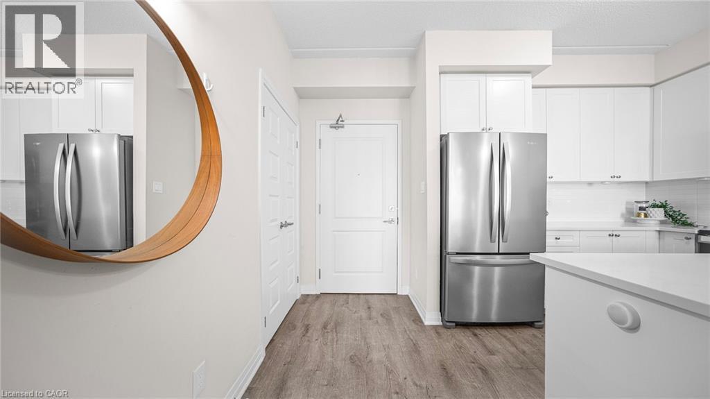 Kitchen featuring white cabinetry, freestanding refrigerator, light wood-style flooring, tasteful backsplash, and a textured ceiling - 610 Farmstead Drive Unit# 304, Milton, ON - Indoor Photo Showing Kitchen With Stainless Steel Kitchen