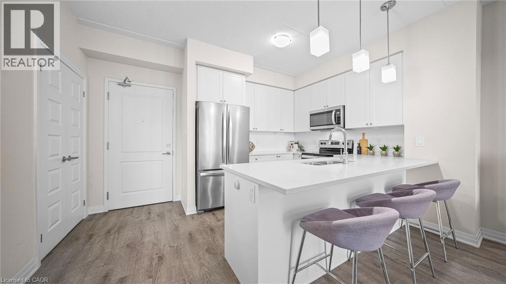 Kitchen featuring appliances with stainless steel finishes, a breakfast bar area, light wood-style flooring, and white cabinets - 610 Farmstead Drive Unit# 304, Milton, ON - Indoor Photo Showing Kitchen With Stainless Steel Kitchen With Upgraded Kitchen