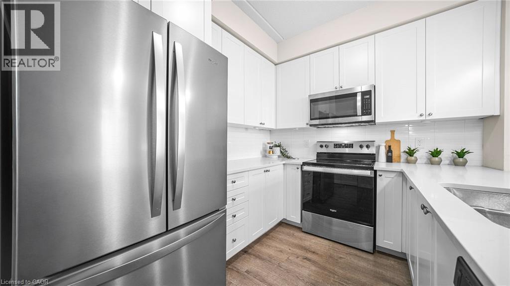 Kitchen featuring appliances with stainless steel finishes, dark wood-style flooring, backsplash, and white cabinetry - 610 Farmstead Drive Unit# 304, Milton, ON - Indoor Photo Showing Kitchen With Stainless Steel Kitchen With Upgraded Kitchen