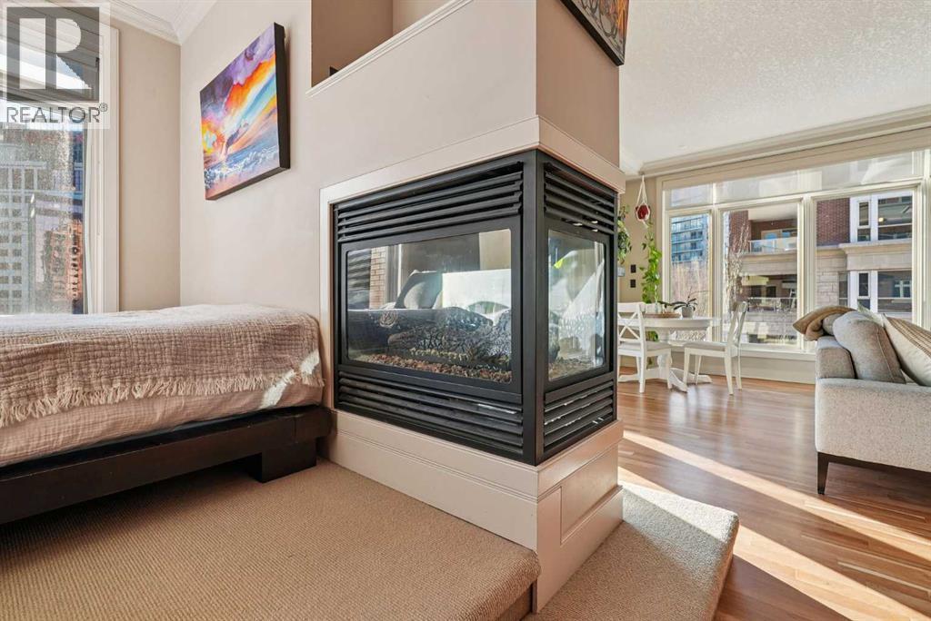 3 sided gas fireplace - 306, 660 Eau Claire Avenue Sw, Calgary, AB - Indoor Photo Showing Bedroom With Fireplace