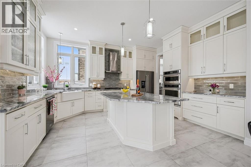 Kitchen featuring glass insert cabinets, appliances with stainless steel finishes, a center island, wall chimney exhaust hood, and light stone countertops - 263 Chestnut Ridge, Waterloo, ON - Indoor Photo Showing Kitchen With Upgraded Kitchen