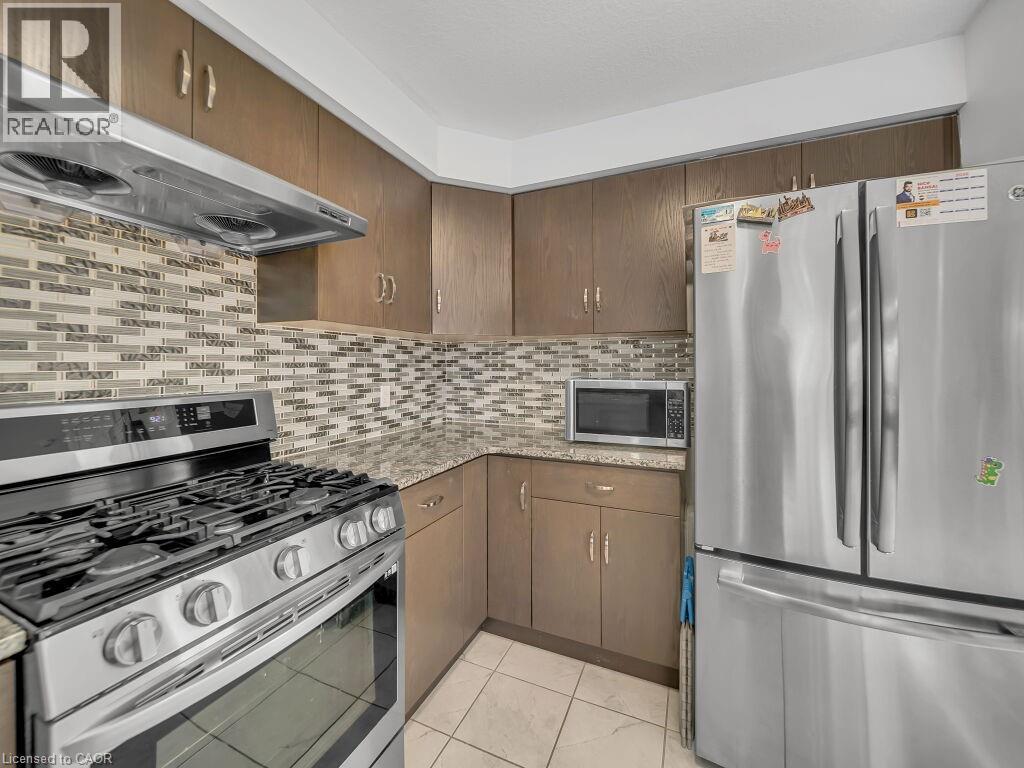 Kitchen with appliances with stainless steel finishes, ventilation hood, light stone counters, backsplash, and light tile patterned flooring - 144 Summit Ridge Drive, Guelph, ON - Indoor Photo Showing Kitchen With Stainless Steel Kitchen With Upgraded Kitchen