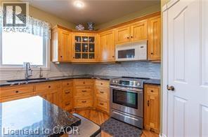 Kitchen with electric range, white microwave, glass insert cabinets, tasteful backsplash, and brown cabinetry - 158 River Run Road, Drayton, ON - Indoor Photo Showing Kitchen