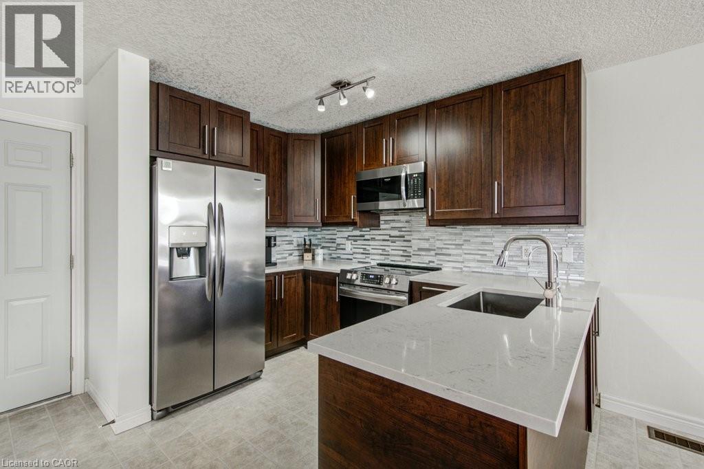 Kitchen featuring appliances with stainless steel finishes, dark brown cabinetry, light stone counters, a peninsula, and tasteful backsplash - 711 Southwood Way, Woodstock, ON - Indoor Photo Showing Kitchen With Upgraded Kitchen