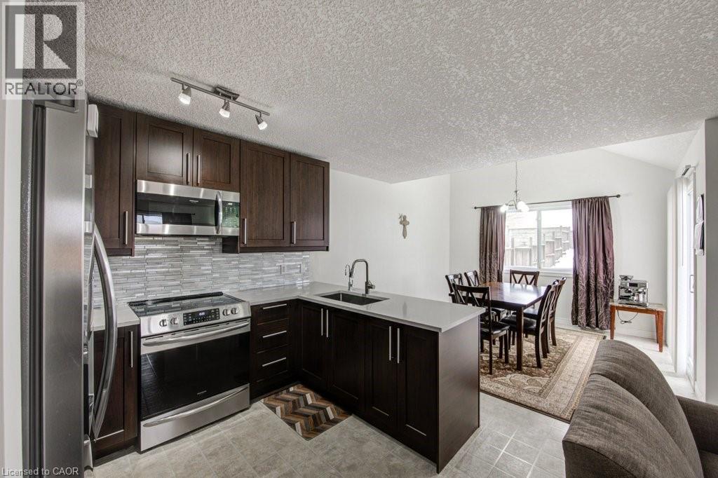 Kitchen featuring stainless steel appliances, dark brown cabinets, a peninsula, backsplash, and a textured ceiling - 711 Southwood Way, Woodstock, ON - Indoor Photo Showing Kitchen With Upgraded Kitchen