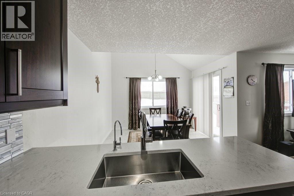 Kitchen with light stone countertops, a textured ceiling, dark brown cabinets, hanging light fixtures, and vaulted ceiling - 711 Southwood Way, Woodstock, ON - Indoor Photo Showing Kitchen With Double Sink
