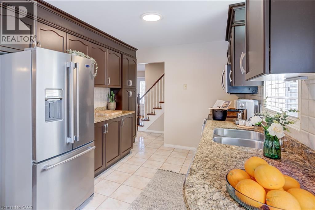 Kitchen featuring appliances with stainless steel finishes, backsplash, light stone counters, dark brown cabinets, and light tile patterned floors - 15 Claudette Gate, Hamilton, ON - Indoor Photo Showing Kitchen With Double Sink