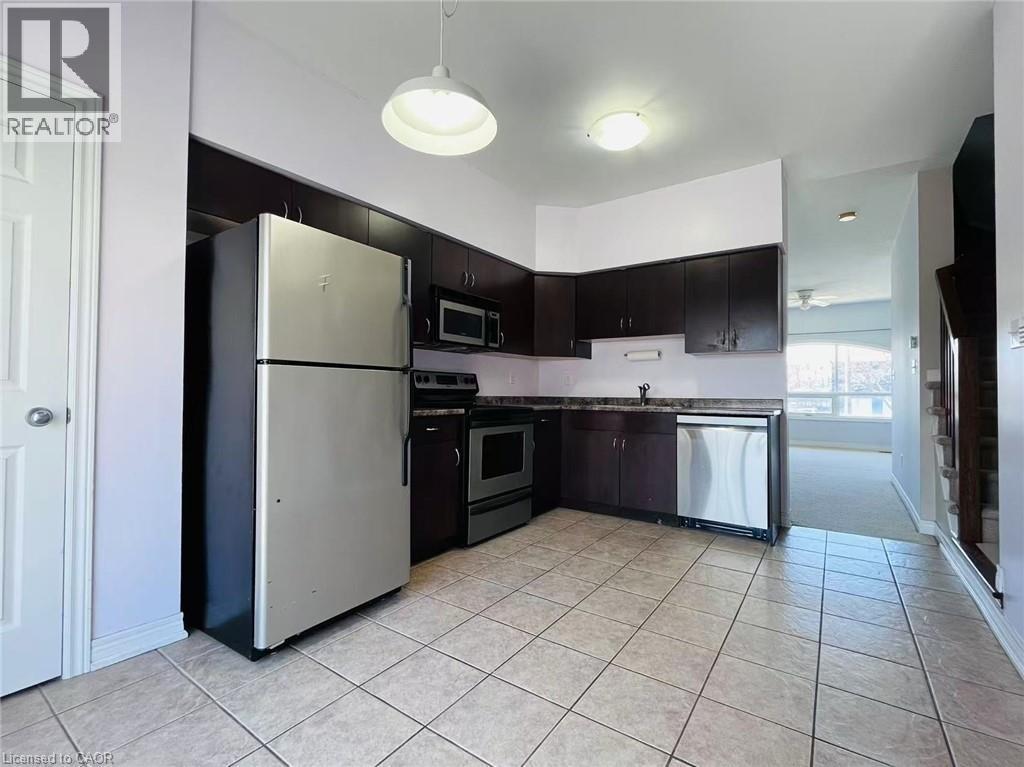 Kitchen with stainless steel appliances, dark countertops, hanging light fixtures, light tile patterned flooring, and dark wood finish cabinets - 5053 Bidwell Common, Burlington, ON - Indoor Photo Showing Kitchen