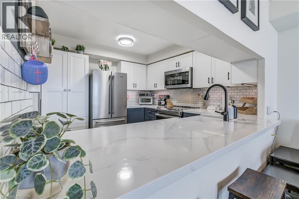 Kitchen with white cabinets, appliances with stainless steel finishes, decorative backsplash, light stone counters, and a kitchen bar - 3845 Lakeshore Boulevard W Unit# 804, Etobicoke, ON - Indoor Photo Showing Kitchen With Stainless Steel Kitchen With Upgraded Kitchen