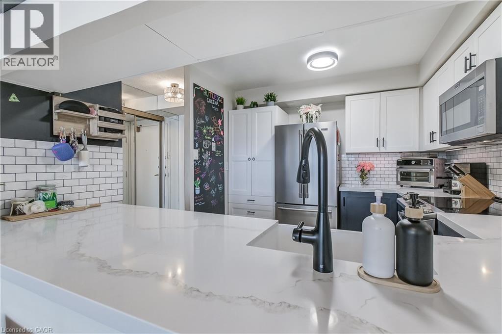 Kitchen with decorative backsplash, white cabinets, appliances with stainless steel finishes, a peninsula, and light stone counters - 3845 Lakeshore Boulevard W Unit# 804, Etobicoke, ON - Indoor