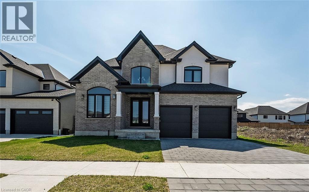 French provincial home with brick siding, decorative driveway, a front lawn, an attached garage, and french doors - 7266 Silver Creek Circle, London, ON - Outdoor With Facade
