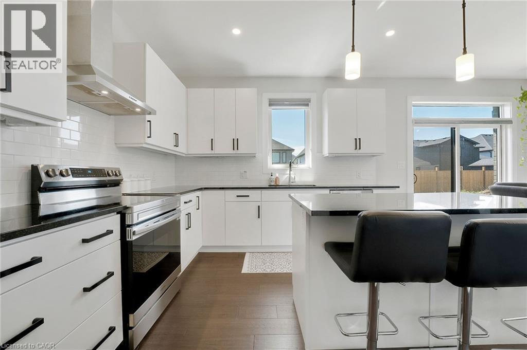 Kitchen with stainless steel electric stove, a kitchen breakfast bar, wall chimney range hood, decorative light fixtures, and dark wood-style flooring - 7266 Silver Creek Circle, London, ON - Indoor Photo Showing Kitchen With Upgraded Kitchen