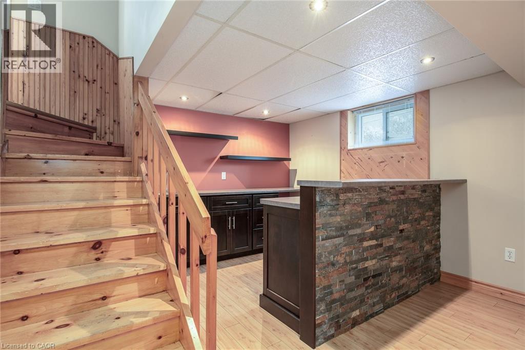 Indoor dry bar featuring stairs, a drop ceiling, dark brown cabinetry, light wood-style flooring, and light countertops - 120 Fourth Avenue, Kitchener, ON - Indoor